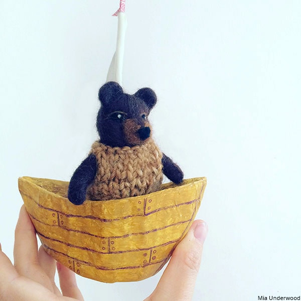 A 3D bear model, created using needle felting, wearing a knitted jumper in a boat