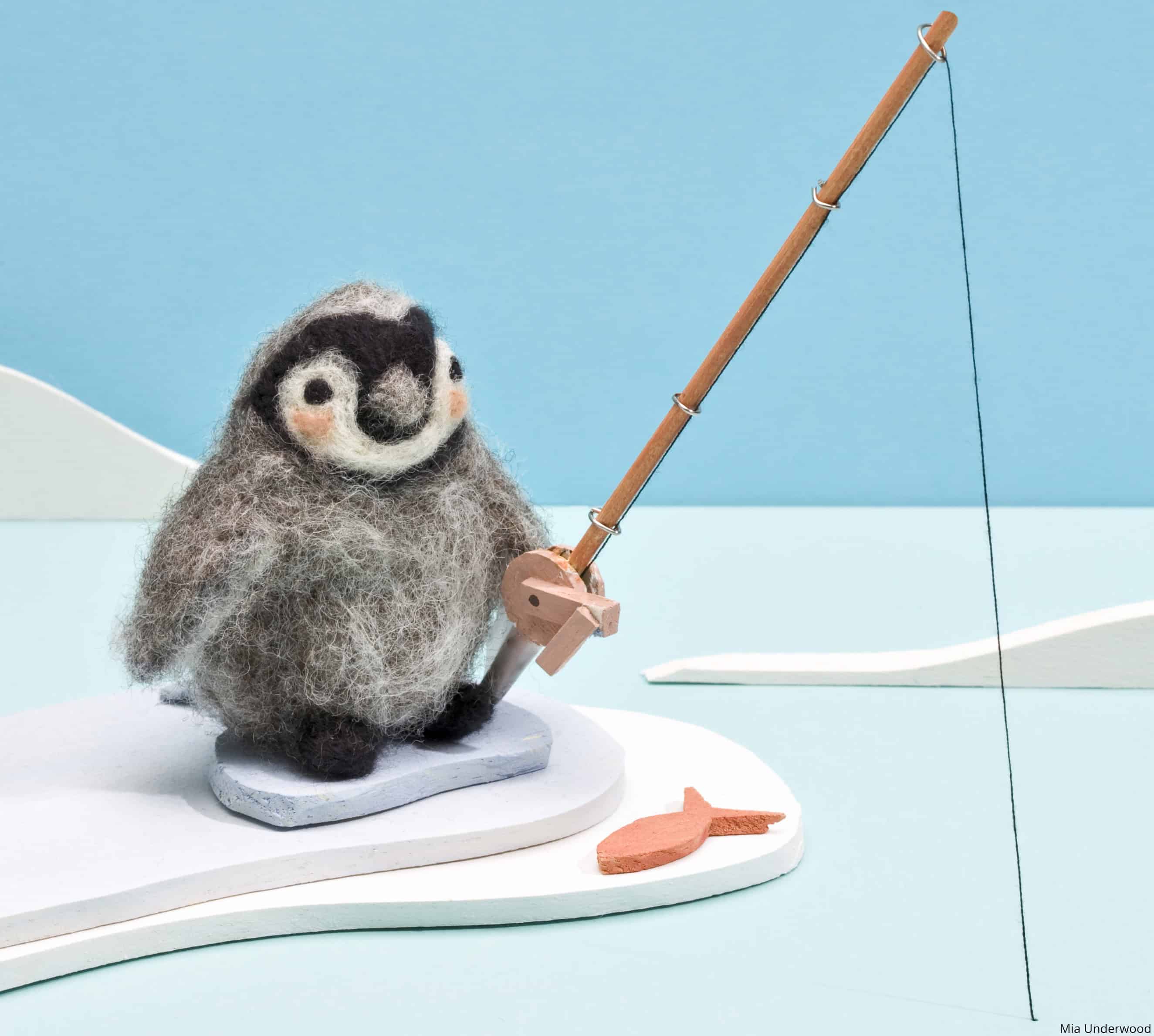 Needle felted penguin 3D figure in an icy scene holding a fishing rod